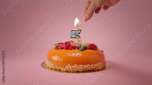 Woman lights candle on Happy 5th birthday cake for birthday party.