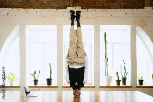 Fotografia Office clerk having fun, doing headstand without hands on wooden table in modern office at work time
