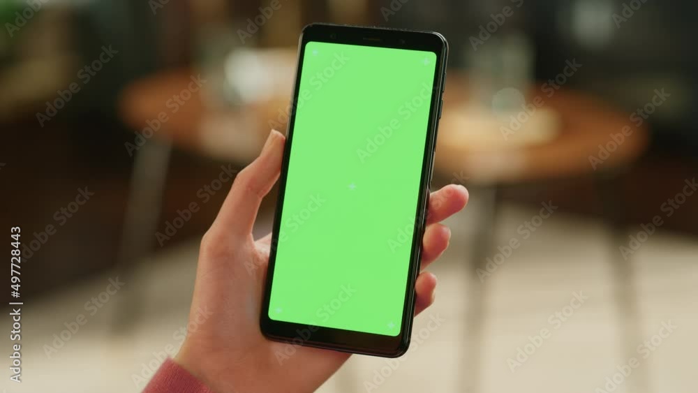 Feminine Hand Holding a Smartphone with Green Screen Mock Up Display. Female is Resting at Home, Watching Videos and Reading Social Media Posts on Mobile Device. Close Up Over the Shoulder Footage.