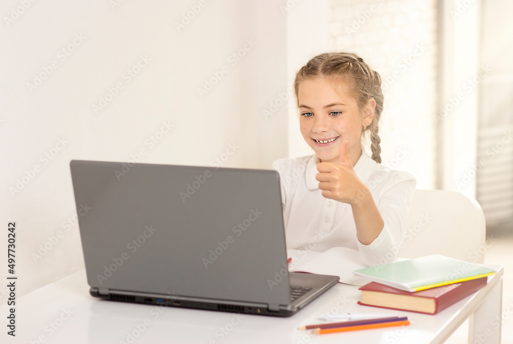 schoolgirl sitting at a table with a laptop and showing thumbs up schoolgirl sitting at a table with a laptop and showing thumbs up