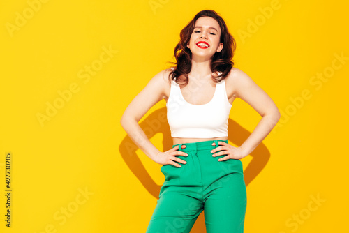 Young beautiful smiling female in trendy summer clothes. Sexy carefree woman posing near yellow wall in studio. Positive model having fun and going crazy. Cheerful and happy. In sunglasses