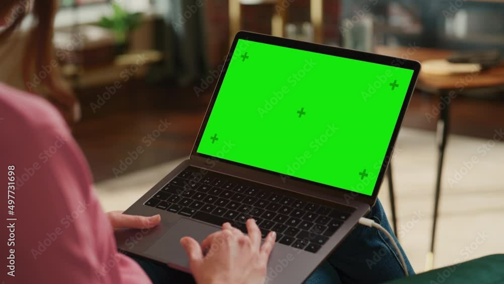 Young Adult Woman Working from Home Loft Apartment on Laptop Computer with Green Screen Mock Up Display. Creative Female Using Trackpad and Browsing Internet. Close Up Over the Shoulder Footage. Young Adult Woman Working from Home Loft Apartment on Laptop Computer with Green Screen Mock Up Display. Creative Female Using Trackpad and Browsing Internet. Close Up Over the Shoulder Footage.