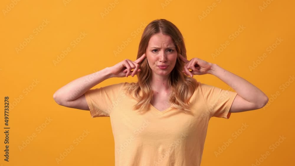 Sad blonde woman wearing yellow t-shirt plugging ears in the orange studio Sad blonde woman wearing yellow t-shirt plugging ears in the orange studio