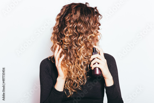 Tablou pe pânză Young woman with brown curly hair applying hair care