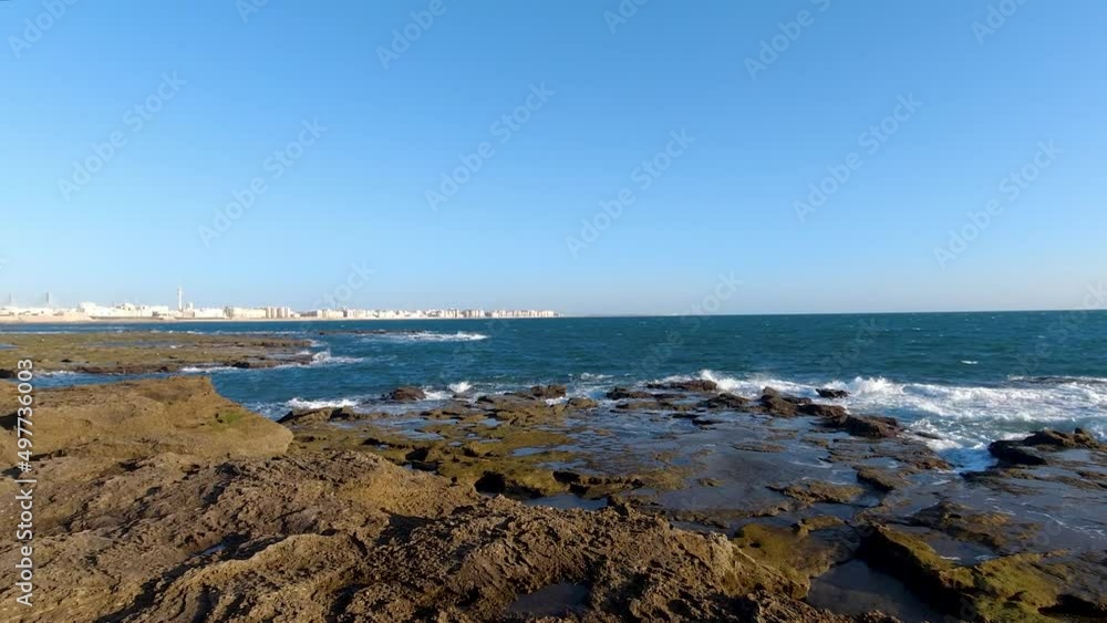Waves breaking in slow motion on rocky beach on clear blue sky day Waves breaking in slow motion on rocky beach on clear blue sky day