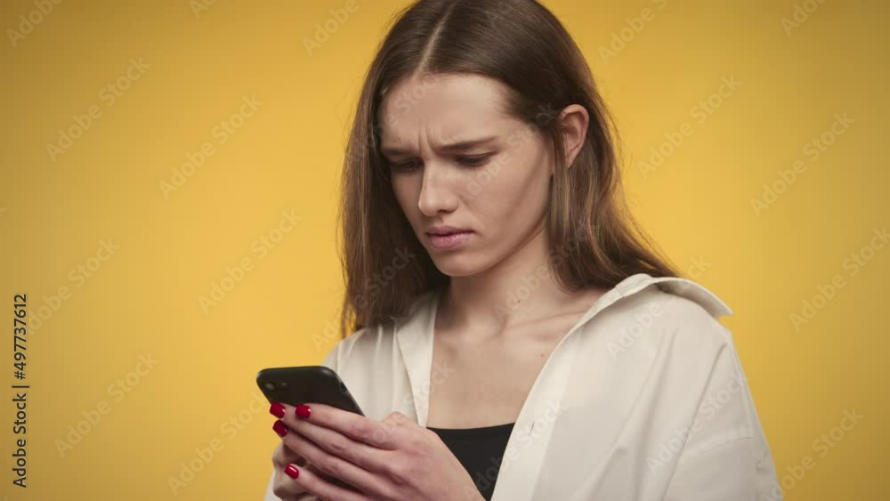 Young adult caucasian woman is texting on her smartphone on a bright yellow background