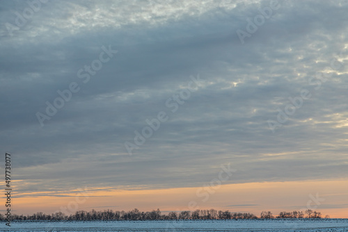 Natural sunset sunrise over field or meadow. The color of the sky over the winter snowy ground. Landscape under a picturesque sky at sunset. Dawn of the sun.