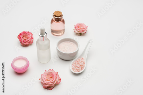 flowers near sea salt, serum and bottle with rose water on white.