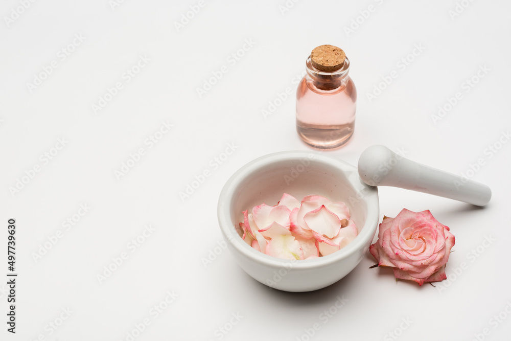 flower near pestle and mortar with petals and bottle with rose water on white. flower near pestle and mortar with petals and bottle with rose water on white.