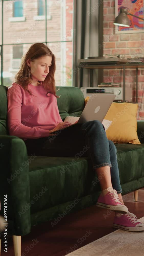 Vertical Screen: Beautiful Female Sitting on a Couch in Living Room, Working from Home on Laptop Computer. Creative Woman Checking Social Media, Browsing Internet. Urban City View from Big Window. Vertical Screen: Beautiful Female Sitting on a Couch in Living Room, Working from Home on Laptop Computer. Creative Woman Checking Social Media, Browsing Internet. Urban City View from Big Window.