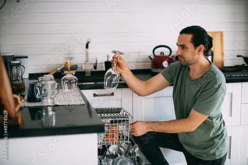 Weekend homework. A young man takes out clean dishes from the dishwasher in the kitchen at home.