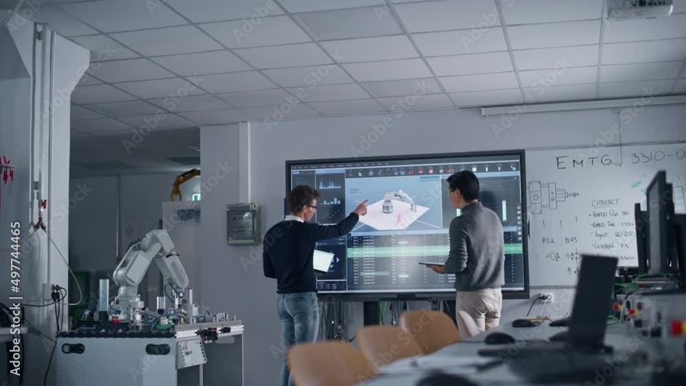 Diverse Team of Two Students Standing Near Big Screen with Tablet and Laptop While Discussing Programming and Technologies. Education and Studying Concept Diverse Team of Two Students Standing Near Big Screen with Tablet and Laptop While Discussing Programming and Technologies. Education and Studying Concept