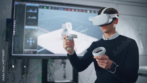 Futuristic University: Caucasian Male Engineer Wearing Virtual Reality Headset Uses Controllers to Remotely Moving Robotic Hand in Special App. Action of Robot Displayed on Screen photo