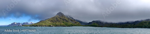 Panorama of a peninsula covered in lush vegetation in front of snow covered mountains at Coopers Bay, South Georgia Island