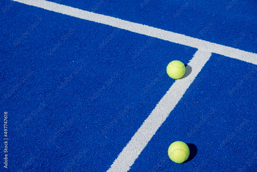 two paddle tennis balls next to the lines of a blue paddle tennis court