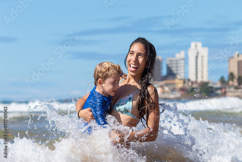 MÃE SORRINDO COM FILHO NA PRAIA.  © Léo