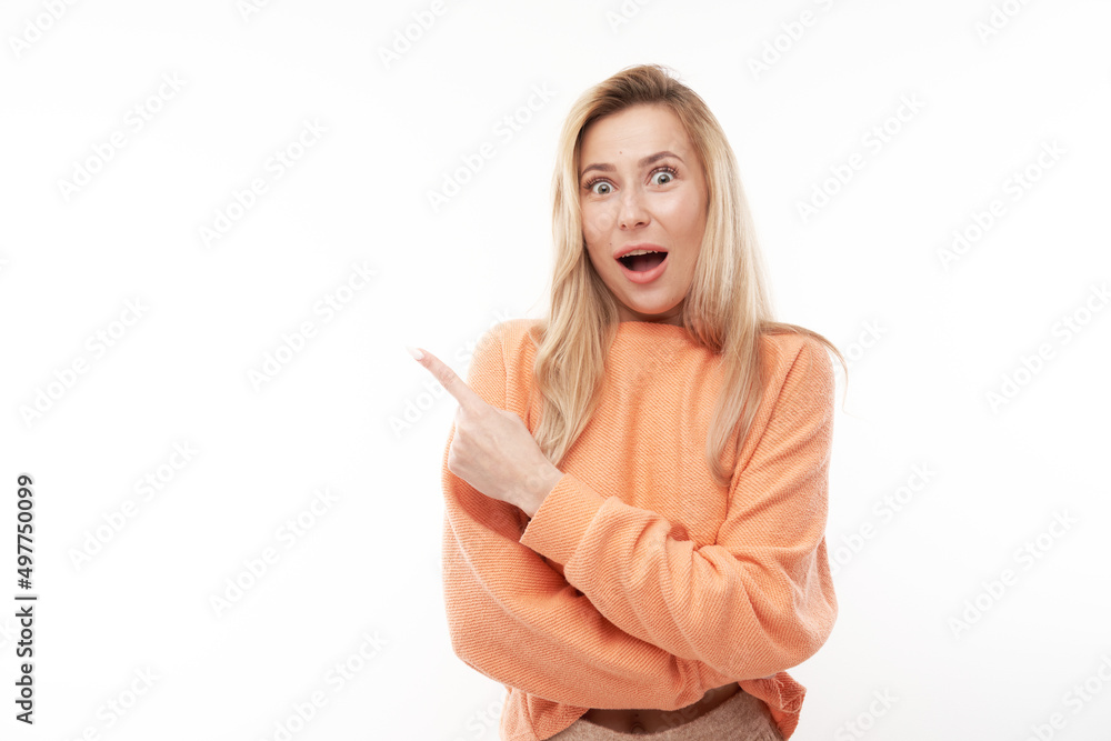 Shocked blond girl looks surprised on white studio background points finger at copy space Shocked blond girl looks surprised on white studio background points finger at copy space