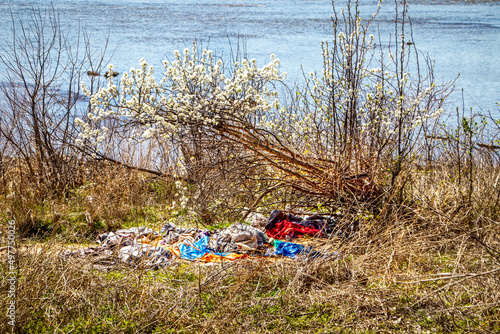 Homeless camp - pile of old clothes piled and spread out under small blooming overhanging tree in early spring down by Arkansas River in Tulsa
