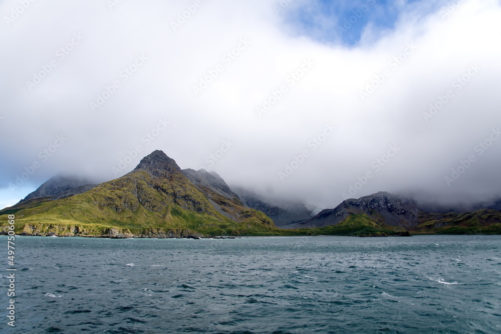 Hills covered in lush vegetation, under low hanging clouds, at Coopers Bay, South Georgia Island