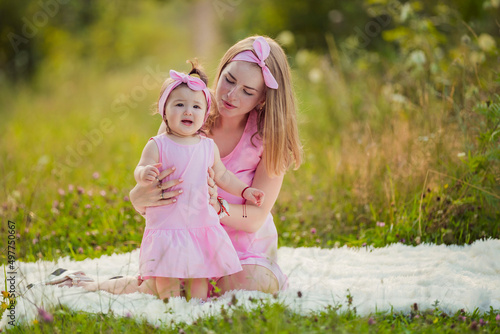 mother and daughter in pink dresses sit on a white blanket © zokov_111