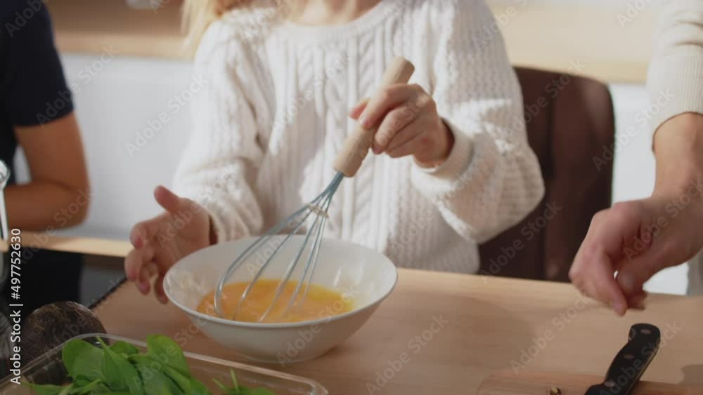 Close up family cooking together. Cute daughter whipping chicken eggs with a hand mixer for cooking stand in kitchen. Breakfast omelette, salad. Slow motion Close up family cooking together. Cute daughter whipping chicken eggs with a hand mixer for cooking stand in kitchen. Breakfast omelette, salad. Slow motion