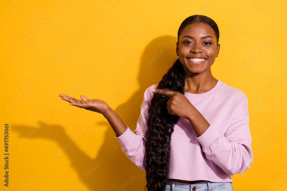 Photo of pretty cheerful girl direct finger hand hold empty space isolated on yellow color background Photo of pretty cheerful girl direct finger hand hold empty space isolated on yellow color background