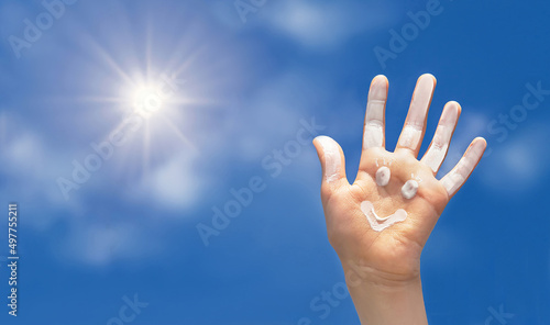 Positive symbol drawing by sunscreen (sun cream, suntan lotion) on open hand on blue sky background. Concept of protection from sun, happy summer vacation.