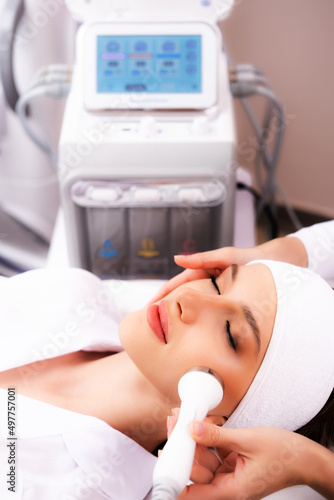 A woman receives ultrasonic cavitation of facial skin against aging. Phonophoresis or ultraphonophoresis apparatus in the hands of a beautician. Clinic of aesthetic cosmetology.