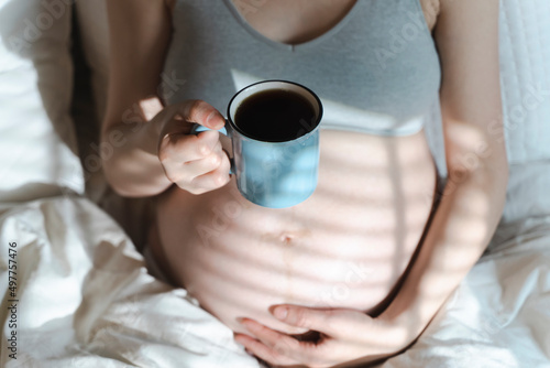 A pregnant woman holds a cup of coffee in her hands. Caffeine safety, myths about coffee during pregnancy concept 