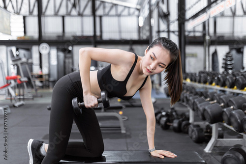 exercise concept The female exercise beginner doing dumbbell workout by resting her left knee and left hand on the bench and raise her right elbow up with a dumbbell in her hand