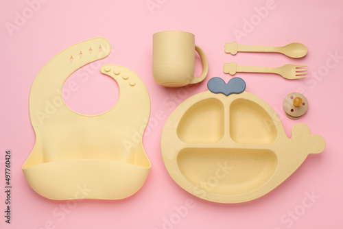 Flat lay composition with baby feeding accessories and bib on pink background