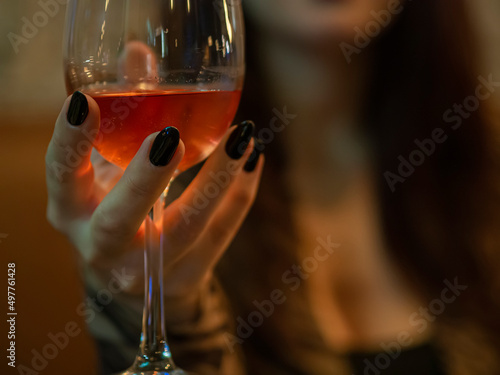 Unrecognizable woman holding a rose wine glass enjoying nightlife. Hand with black nails on a date in a restaurant drinking wine. Carefree and sensuality concept. Toasting in a bar to celebrate