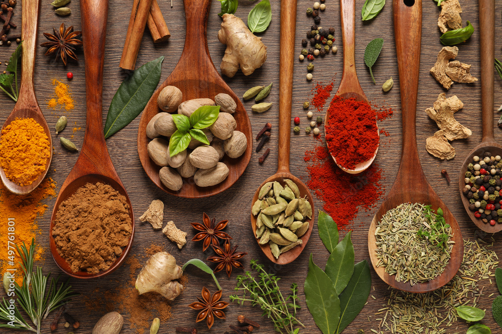 Different herbs and spices with spoons on wooden table, flat lay