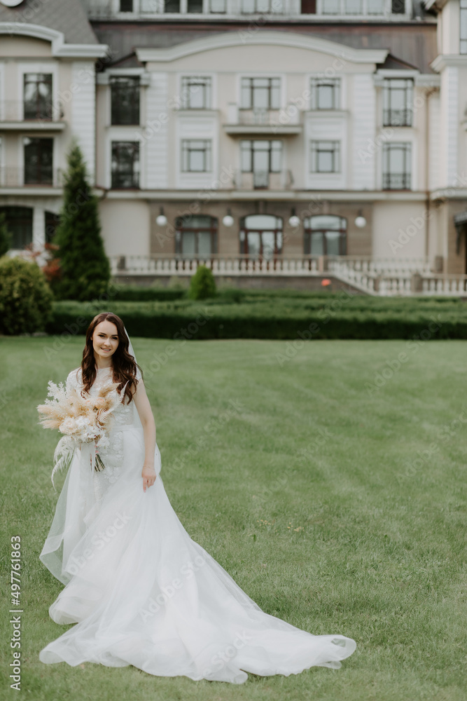 bride in a dress standing in a green garden and holding a wedding bouquet of flowers and greenery