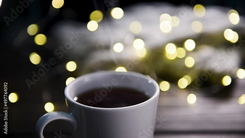 A cup of hot coffee, shot close-up with selective focus. Steam rises from a mug of tea against the backdrop of a garland.