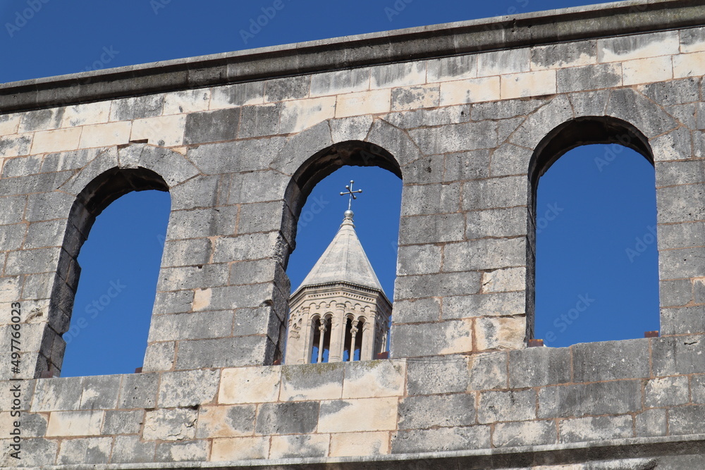 Stone wall with arches and bell tower of Diocletian Palace in Split, Dalmatia, Croatia against a bright blue sky