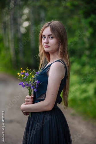 Portrait of a Russian girl with a bouquet of wild flowers in the evening at the village.
