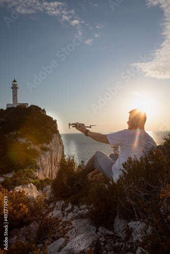 man with drone at the cliff near sea sunset above the lighthouse