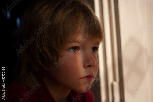 dramatic portrait of an upset lonely boy of 6 years old in a dark room, accentuated by a streak of light. hope and faith, dreams and feelings of a child