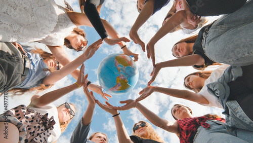 Earth conservation concept. 11 girls surround the rotating earth globe with their palms. photo