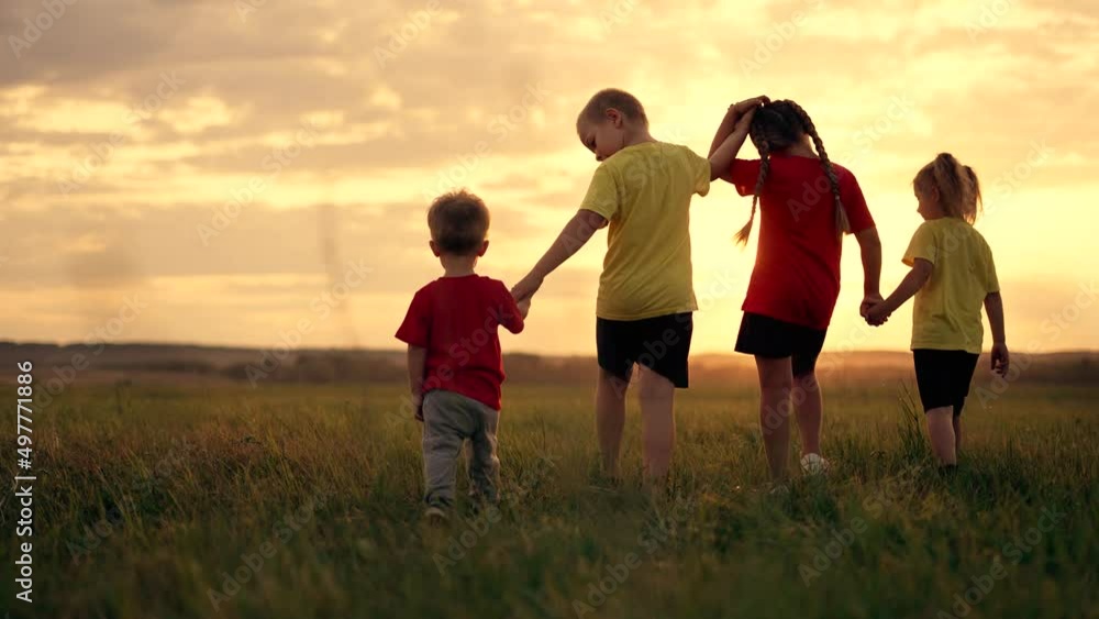 Happy family. Children holding hands walk on green grass. Happy children play at sunset in the park. Cheerful children walk in the field. Active lifestyle. Family picnic on green grass. Dream concept Happy family. Children holding hands walk on green grass. Happy children play at sunset in the park. Cheerful children walk in the field. Active lifestyle. Family picnic on green grass. Dream concept