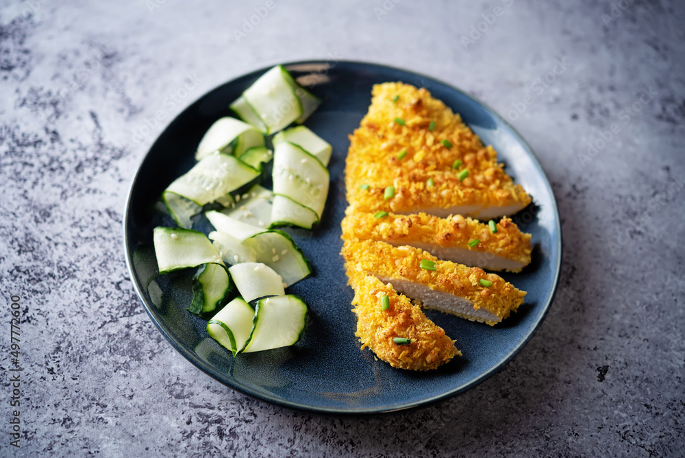 Bread crumbs cheesy chicken breast with cucumbers in a plate