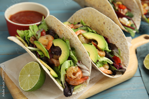 Delicious tacos with shrimps, avocado and lime on turquoise wooden table, closeup