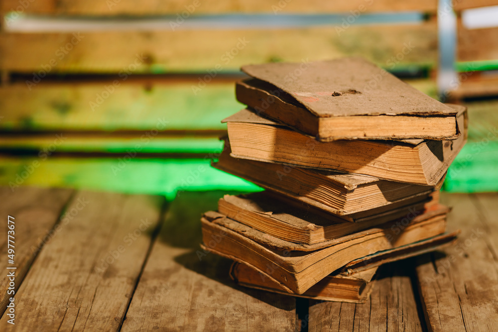 Stack of very dusty, antique books on wooden board with blurred background