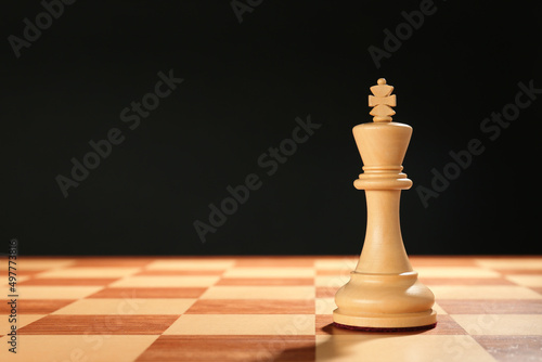 Wooden king on chessboard against dark background, space for text