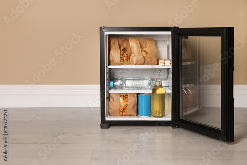 Mini bar filled with food and drinks near beige wall indoors, space for text