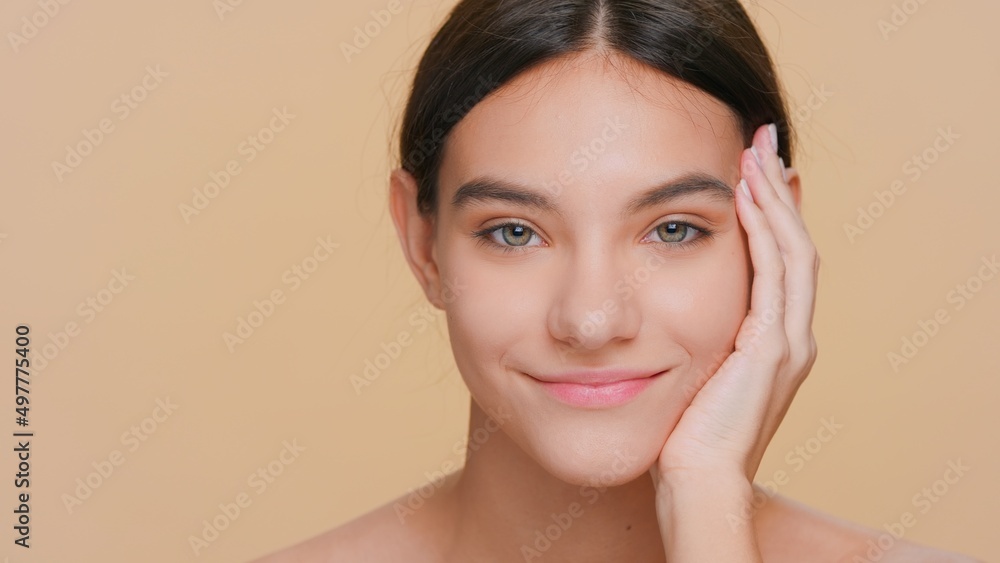Beauty portrait of young dark-haired woman who looks at camera and puts palm on her cheek Beauty portrait of young dark-haired woman who looks at camera and puts palm on her cheek