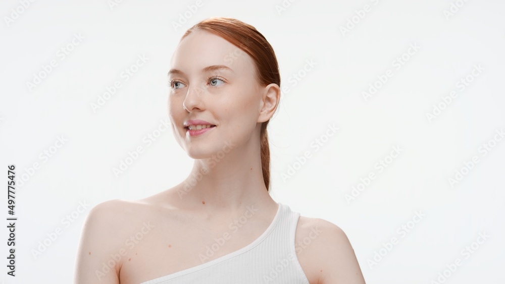 Medium close-up beauty portrait of young redhead woman in white top looking aside and smiling on white background | Skin care commercial concept Medium close-up beauty portrait of young redhead woman in white top looking aside and smiling on white background | Skin care commercial concept