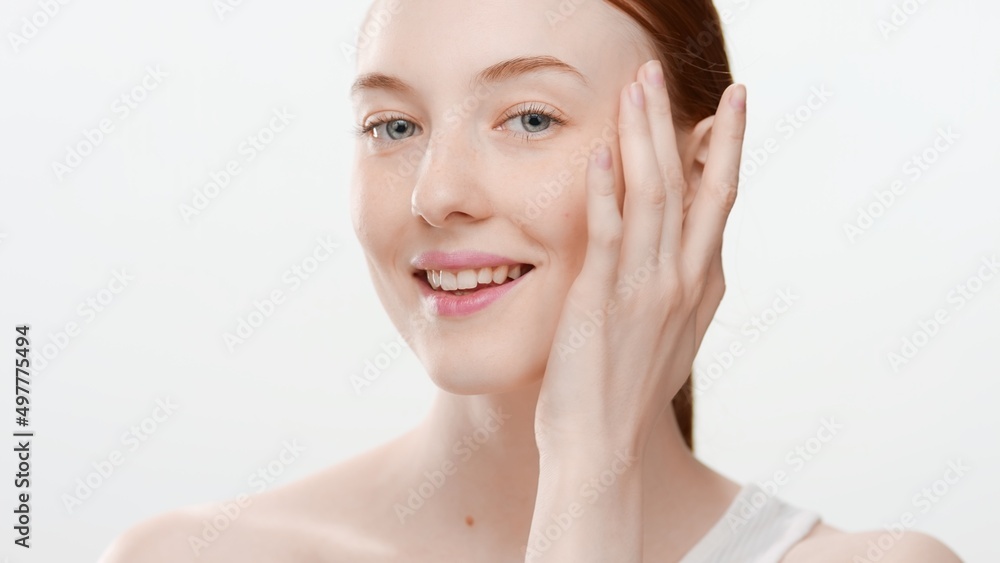 Beautiful Caucasian slim young ginger woman touches her cheek smiling wide for the camera on white background | Skin and beauty care concept Beautiful Caucasian slim young ginger woman touches her cheek smiling wide for the camera on white background | Skin and beauty care concept