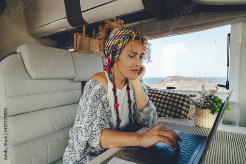 Attracive young adult woman using laptop computer inside camper van alternative office. People and digital nomad or smart working activity lifestyle. Van life and travel for work. Online job activity